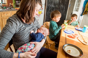 woman breastfeeding infant with two toddlers at the table