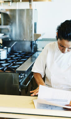 person in commercial kitchen looking at notes