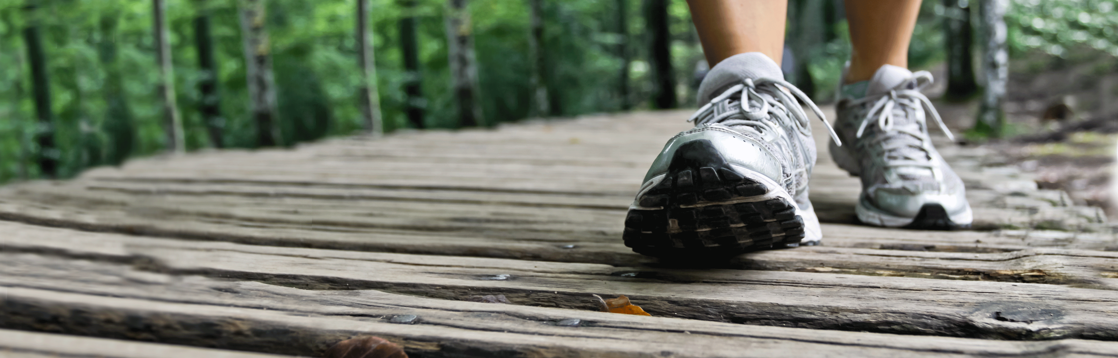 A person wearing sneakers, walking on a trail bridge. 