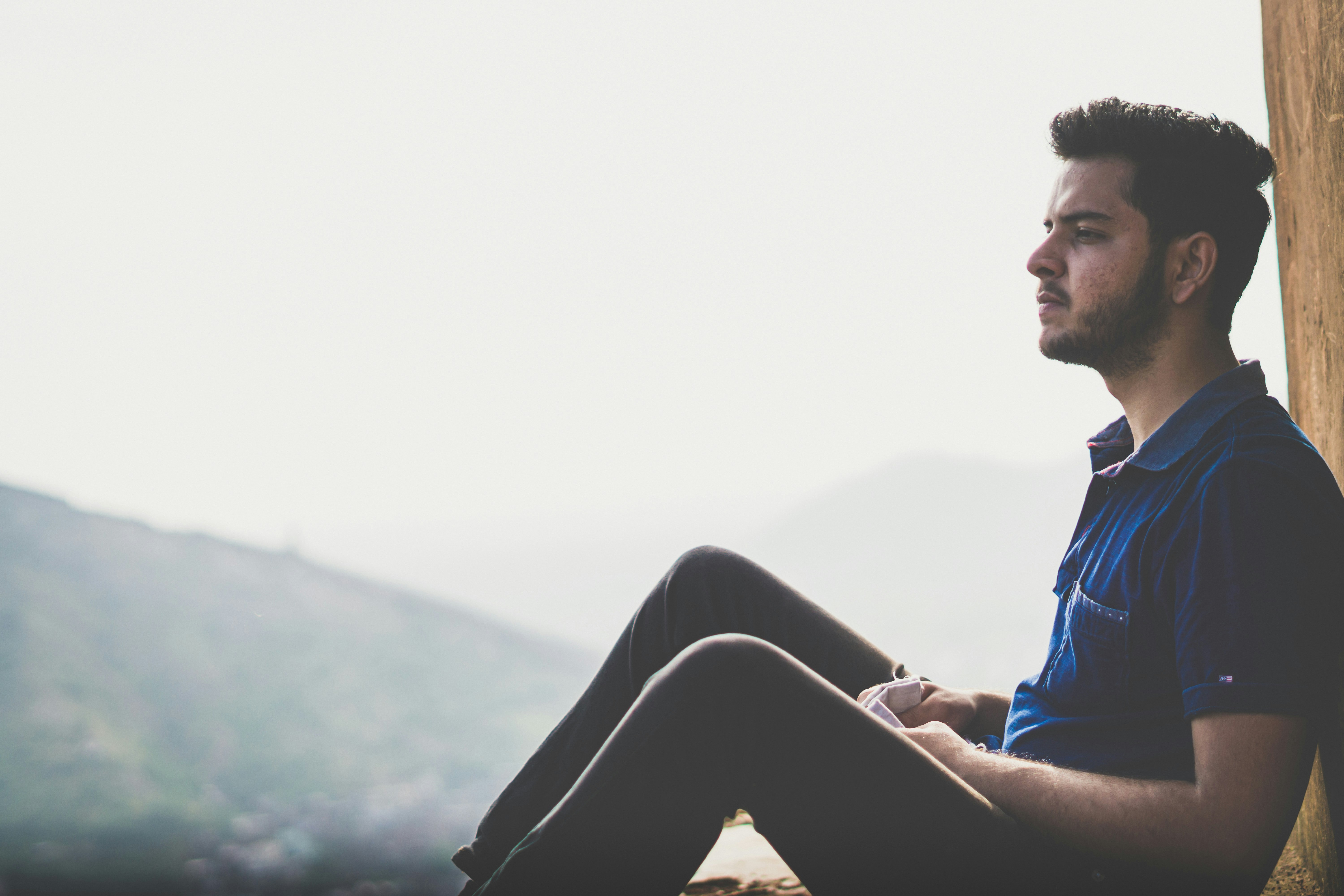 Man leaning against a wall with mountains in the background.