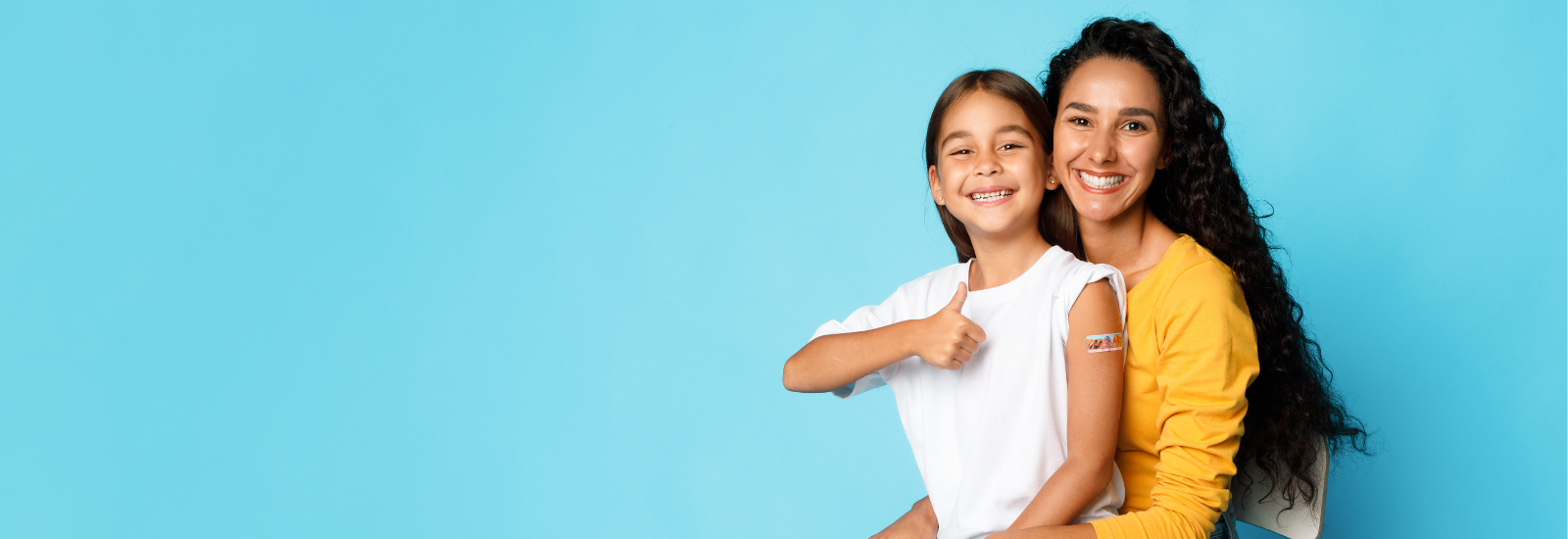 Mom holding her child on her lap while the child with a Band-Aid on their arm, gives a thumbs up.