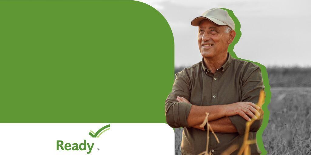 Man standing in a field, smiling with his arms comfortably crossed.