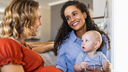 portrait of pregnant person talking with another person holding a baby