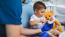 Dental hygienist showing young child and teddy bear how to brush teeth