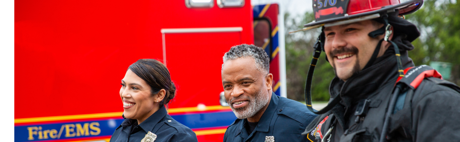 Two paramedics and a firefighter, smiling next to a red emergency vehicle.