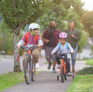 two kids on bikes, parents trotting behind