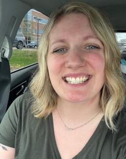 A blonde woman sitting in a car smiling at the camera.