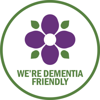 Dementia friendly communities' logo with a purple flower and slogan We're Dementia Friendly.