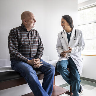 A health care provider sitting next to a man on an exam table (large)